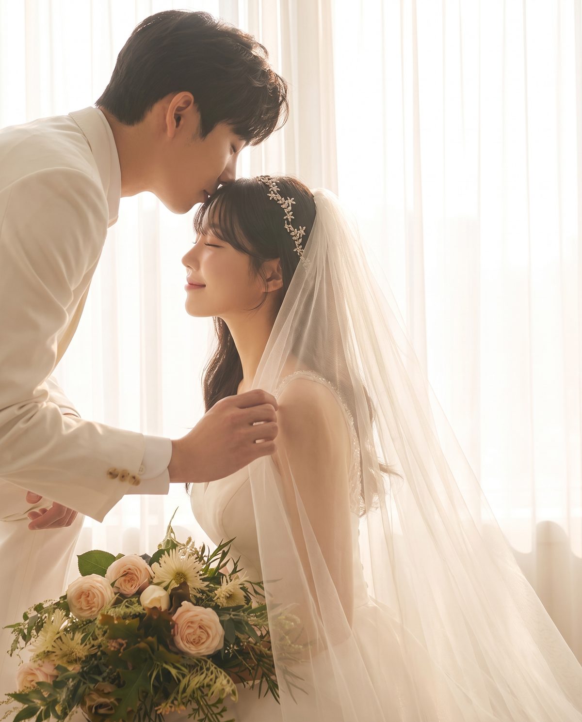 커튼 빛 아래 이마에 입 맞추는 신랑과 면사포를 쓴 신부
